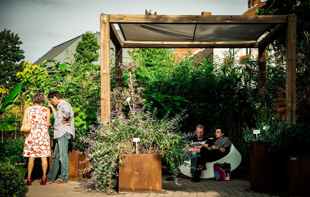Menschen sitzen in einem Garten unrter einer Terrassenüberdachung aus Holz 
